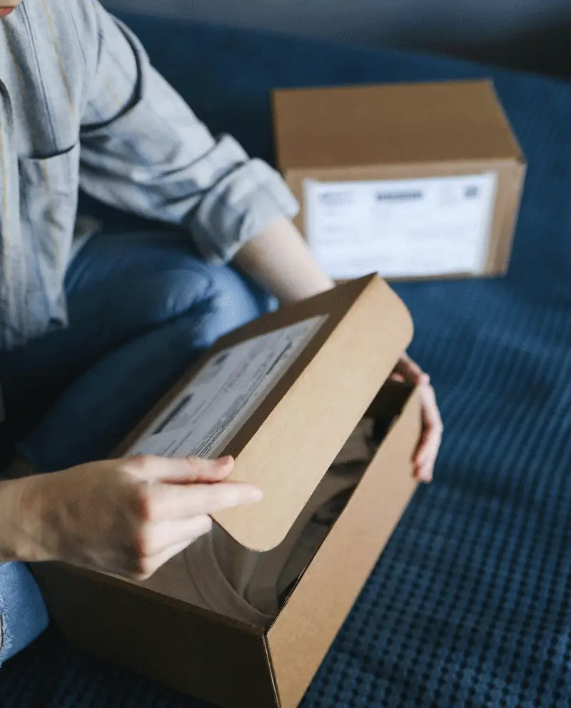 Person opening a cardboard shipping box during last-mile delivery on a blue bedspread